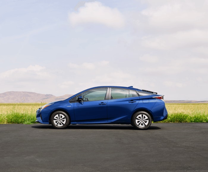 Lateral exterior view of the Toyota Prius Two in blue while parked next to a green field. 