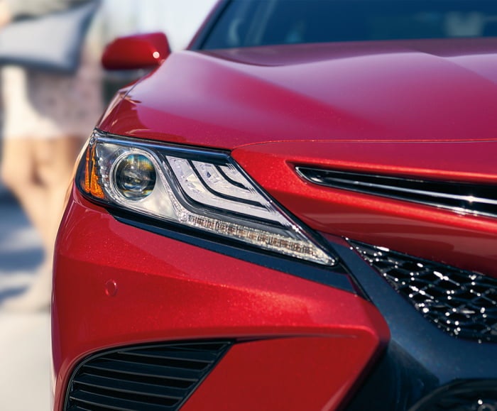 Front-facing shot of static headlight and front bumper of 2018 Camry in Supersonic Red.