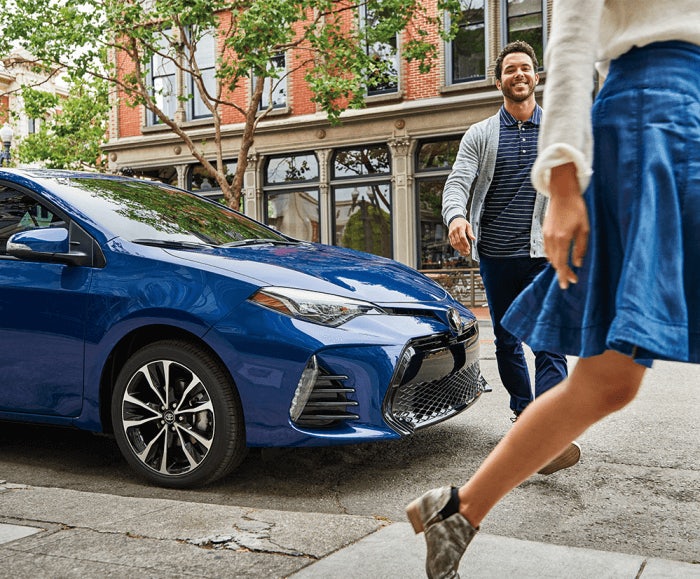 Side-facing shot of the 2017 Toyota Corolla SE in Blue Crush Metallic parked on a city street with people walking by.