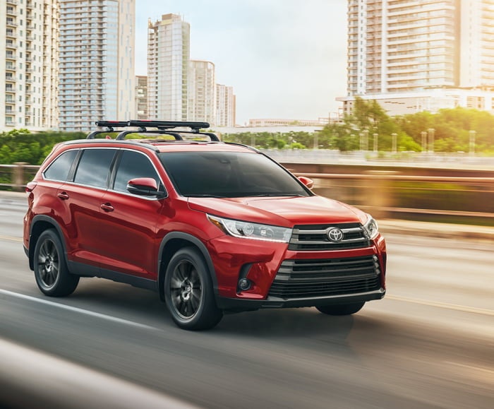 Action-Perfomance shot of the 2019 Highlander SE in Salsa Red Pearl on a bridge with body of water and city in background.