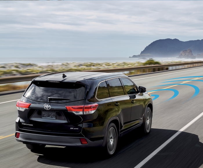 Rear-angled shot of the 2018 Highlander SE in Midnight Black Metallic using sonar with the 2018 Highlander Hybrid in Blizzard Pearl driving in front. 