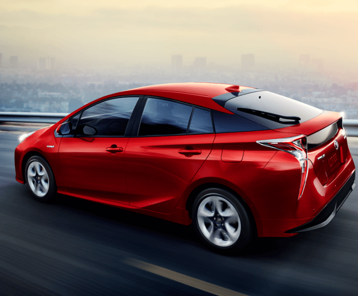 Rear angled view of the Prius Four Touring in red being driven on a city highway with an urban landscape in the background.