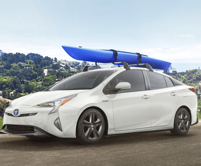 Exterior view of the Prius Four Touring in white with a blue kayak on its roof. The Prius Four Touring is parked overlooking a large lake and green hills.