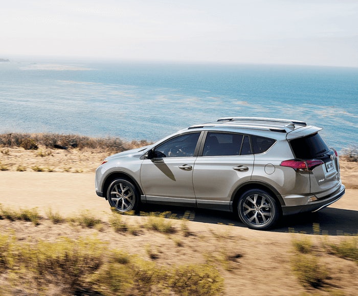 Rear angled shot of the RAV4 SE in Blizzard Pearl cruising along a dirt path hugging the coastline.