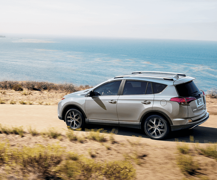 Rear angled shot of the RAV4 SE in Blizzard Pearl cruising along a dirt path hugging the coastline.