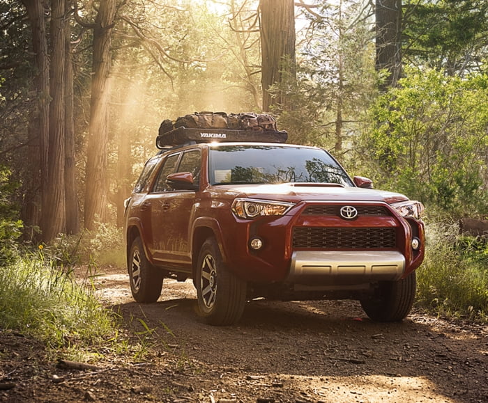 7/8 front passenger side shot of 2019 4Runner in Barcelona Red Metallic driving on forest road.