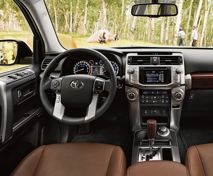 Wide interior shot of dashboard with leather-trimmed seats of 2019 4Runner. View from windshield of campers pitching tent outside.