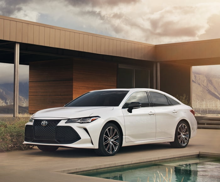 Driver side exterior view of 2019 Avalon Touring in Wind Chill Pearl parked in a driveway in front of a residence.