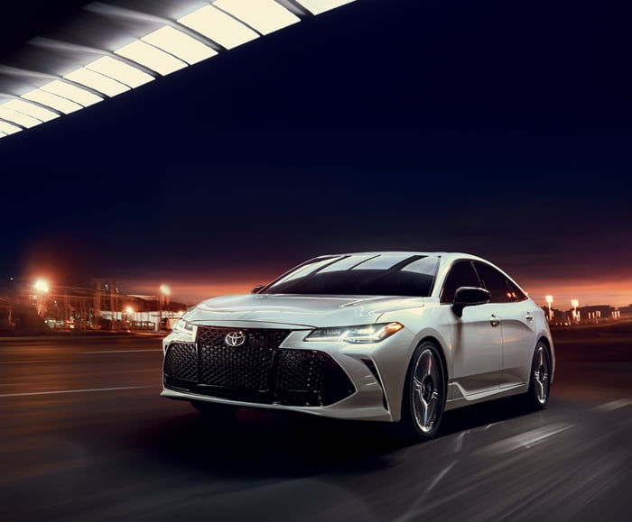 Driver side exterior view of 2019 Avalon in Celestial Silver Metallic driving down city street at night.