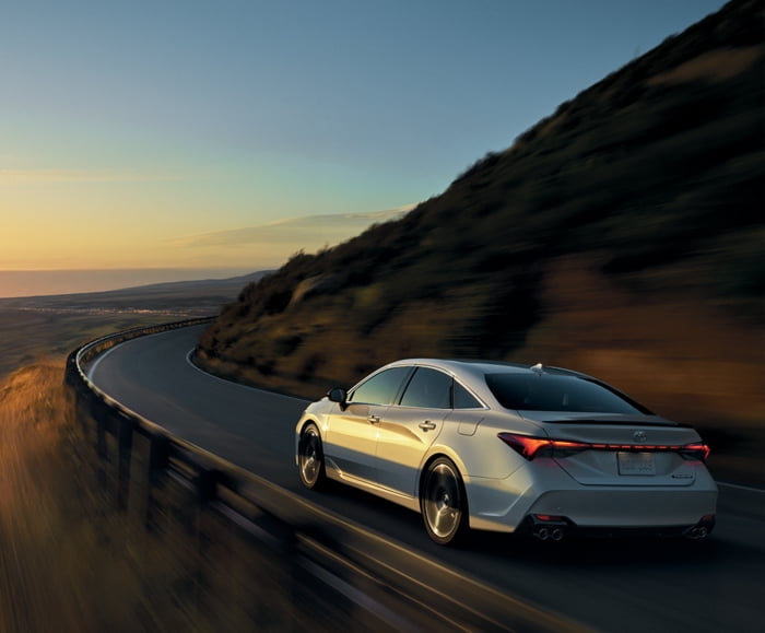 Rear 3/4 driver side exterior view of 2019 Avalon Touring in Wind Chill Pearl driving on road.