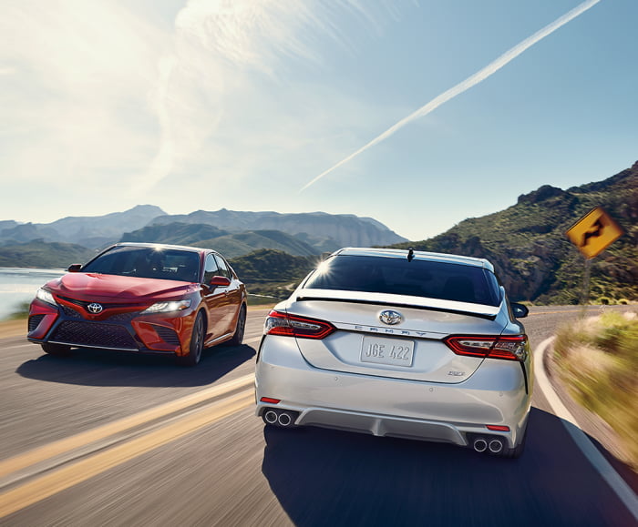 Beauty Shot of two Camrys on an open road, one in Ruby Flare Pearl, the other in Wind Chill Pearl with Midnight Black Metallic Roof.