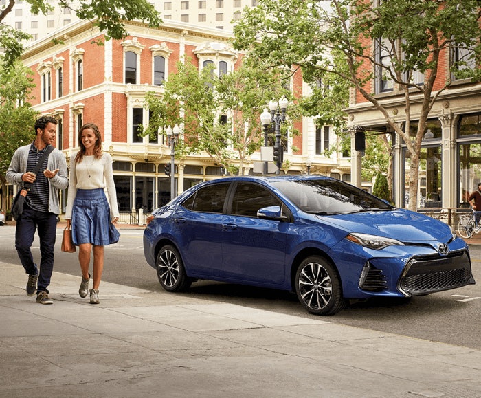Side-angled view of the 2017 Toyota Corolla SE in Blue Crush Metallic parked on a city street with a young couple walking by. 