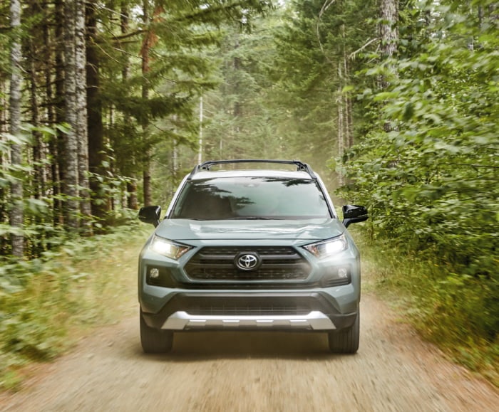 Adventure grade head on shot driving down a forested dirt road.
