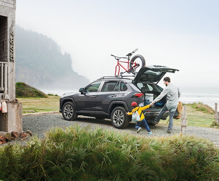 Adult male with male child in front of 2019 RAV4 in Magnetic Grey Metallic parked in front of house on the beach. 