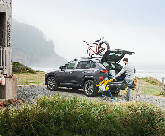 Adult male with male child in front of 2019 RAV4 in Magnetic Grey Metallic parked in front of house on the beach.