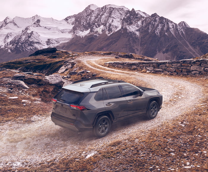 Passenger side view of 2019 RAV4 in Magnetic Grey Metallic on dirt road driving towards mountains.