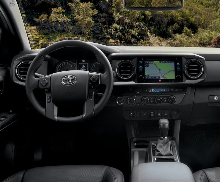 Interior front-facing shot of the Toyota Tacoma TRD Pro in black with steering wheel and infotainment system in view. 