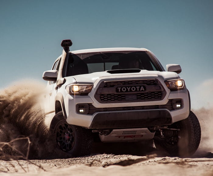 Front-facing shot of the Toyota Tacoma TRD Pro in Super White driving through a desert landscape. 