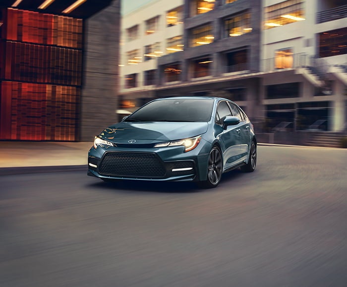 Exterior front 7/8 view of 2020 Corolla XSE in Celestite Gray Metallic on city road in front of buildings.