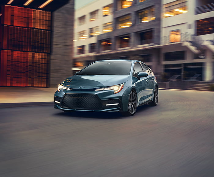 Exterior front 7/8 view of 2020 Corolla XSE in Celestite Gray Metallic on city road in front of buildings.